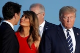 Melania Trump, wearing a red dress, smiles as she leans in to kiss Canadian PM Justin Trudeau on the cheek.