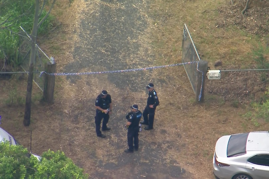 Aerial view of three police standing at a farm gate marked off with police tape