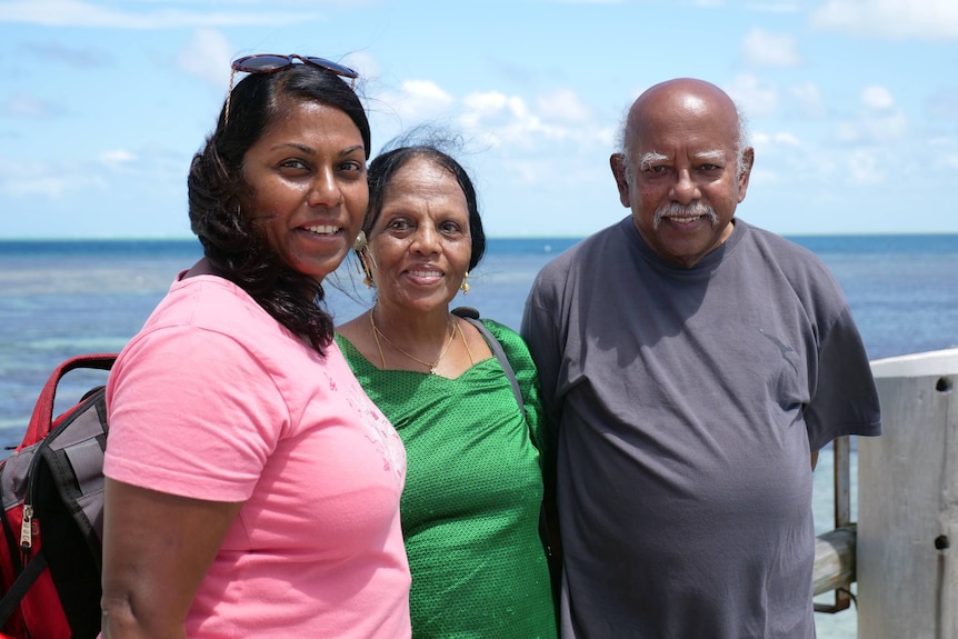 Priya, Meshach and Chellam standing together smiling, ocean behind.
