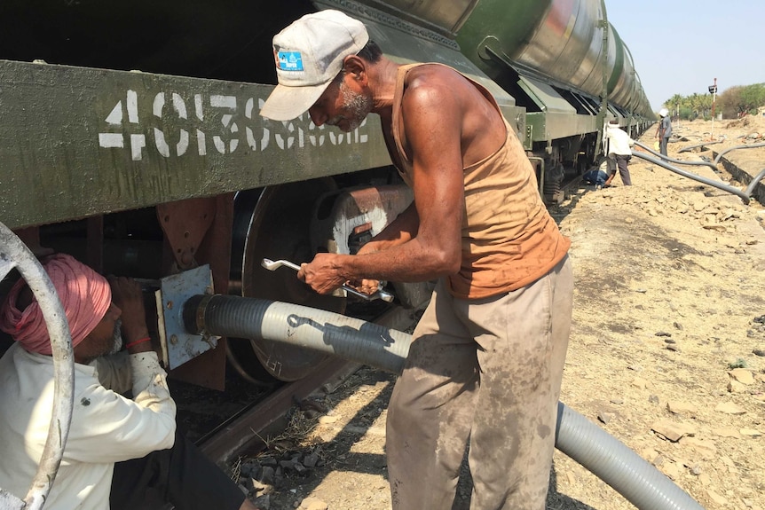 Workers connect hoses to empty the train's wagons.