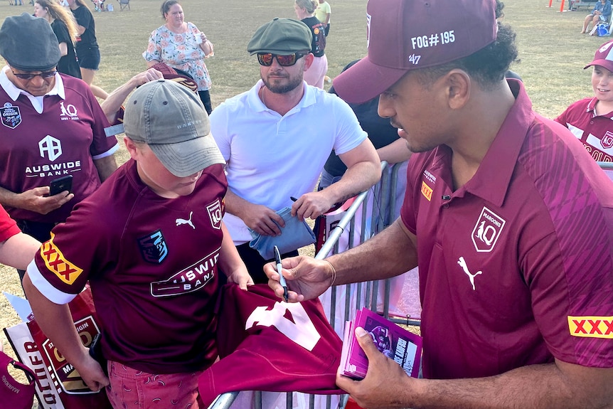 A man signing a queensland maroons uniform.