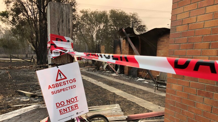 A sign in front of a burnt building says 'Abestos suspected. Do not enter'