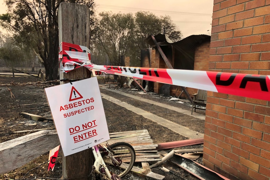 A sign in front of a burnt building says 'Abestos suspected. Do not enter'