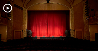 Empty, darkened theatre with closed, red curtains across the stage.