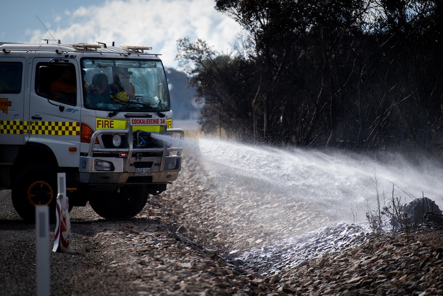 A white Country Fire Service truck with orange and yellow reflective tape sprays water on the fireground.