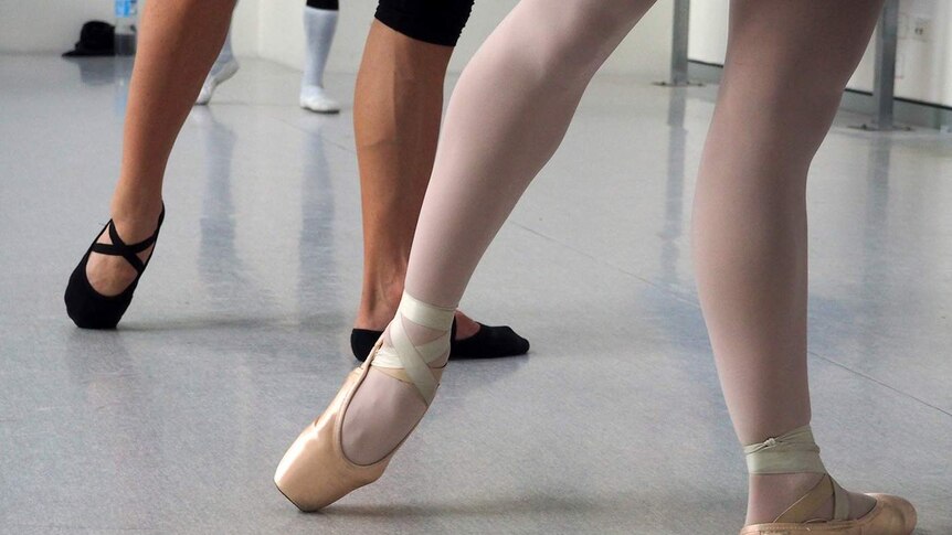 Two pairs of feet and legs in a ballet studio.