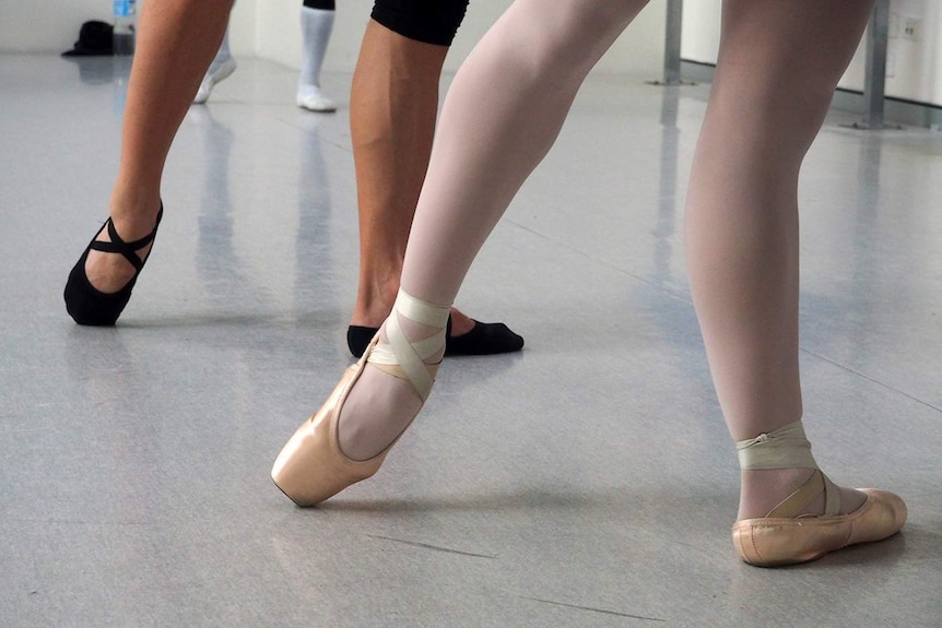 Two pairs of feet and legs in a ballet studio.