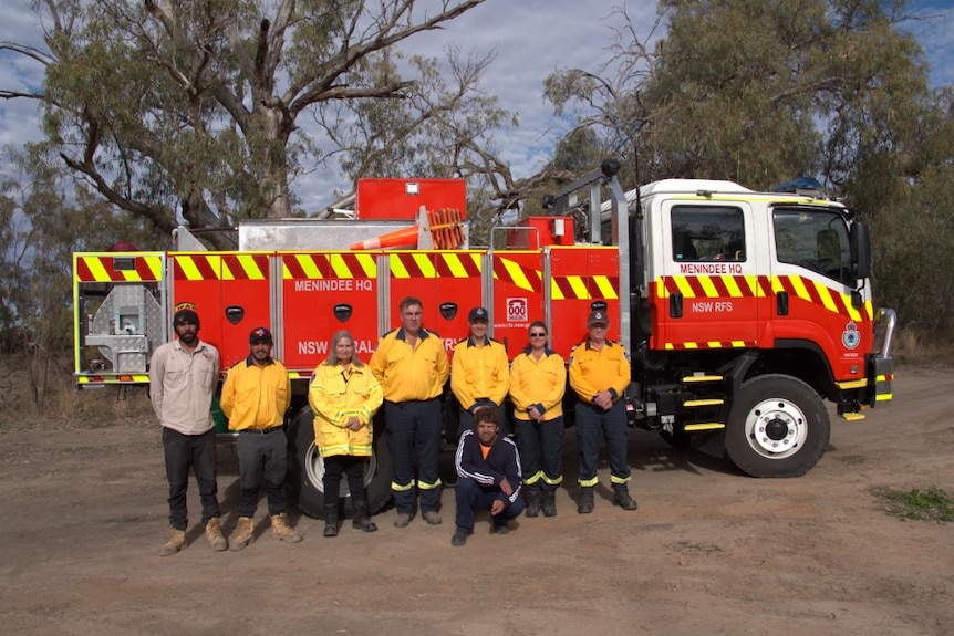 Seven people wearing yellow fire jackets, and one Indigenous man in blue stand in front of a new fire truck
