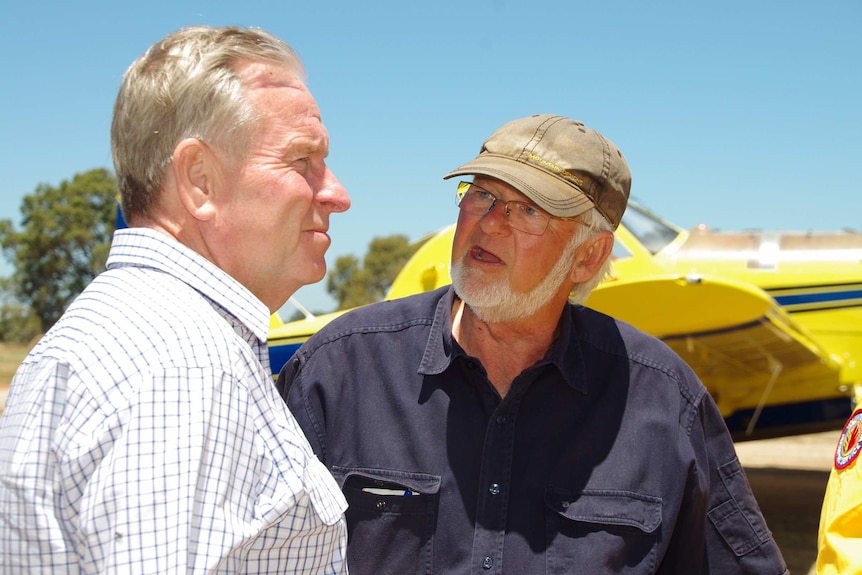 A man talks to the premier with a yellow plane int he background.