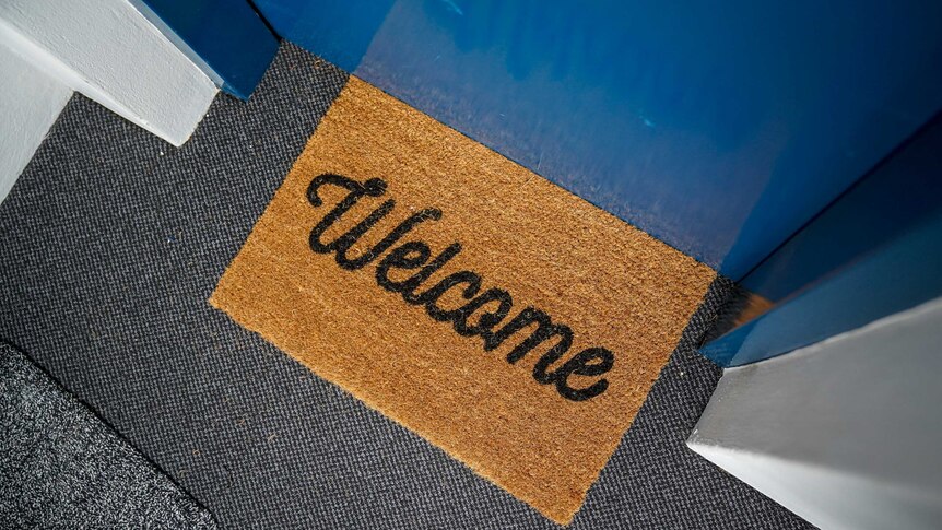 A welcome mat sits on the floor outside a blue door in a Sydney apartment building.