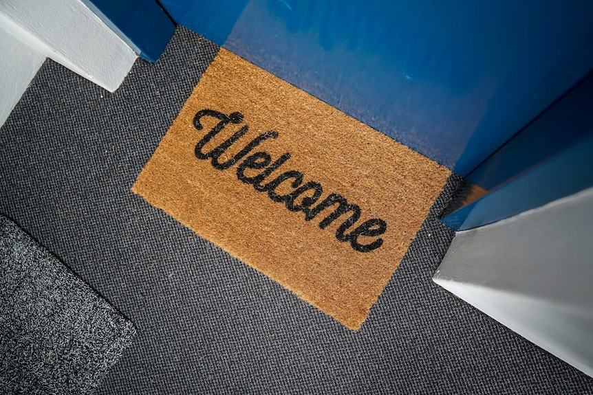 A welcome mat sits on the floor outside a blue door in a Sydney apartment building.