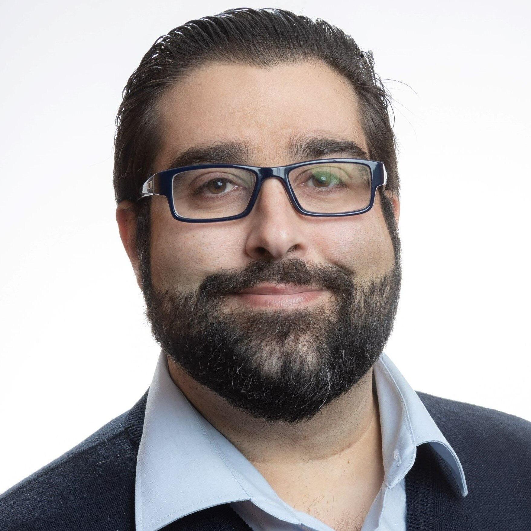 a headshot of a middle-aged man with black hair and a beard, wearing glasses