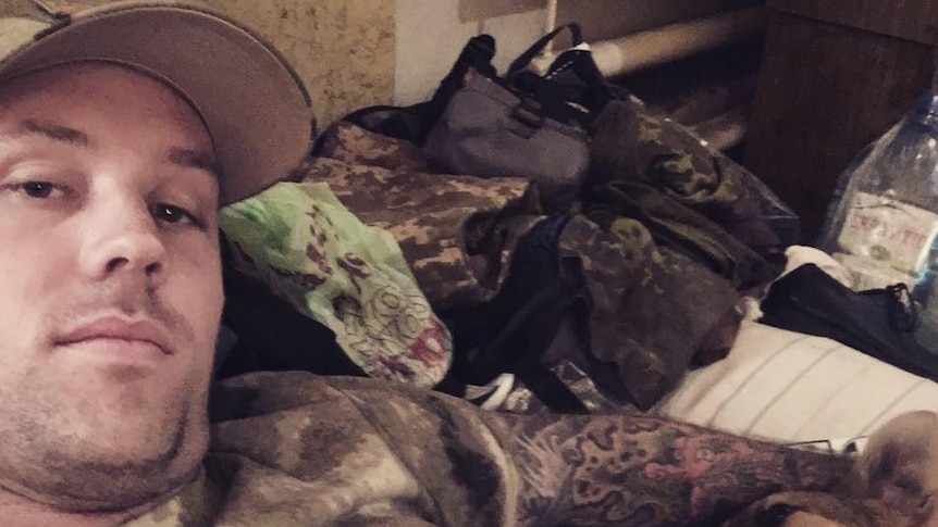 Seorang pria berpakaian kamuflase berbaring dengan seekor anjing.