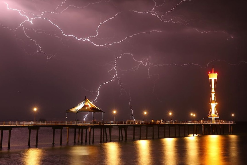 Lightning at night above a jetty with a tower looking like a ship's crows nest