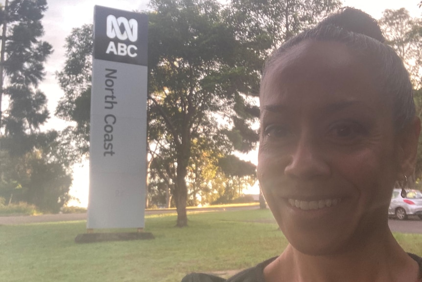 A woman smiles as she stands in front of a sign that reads ABC North Coast