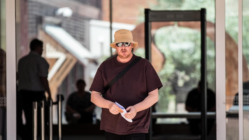 A man wearing a hat and sunglasses walking out of a court building.
