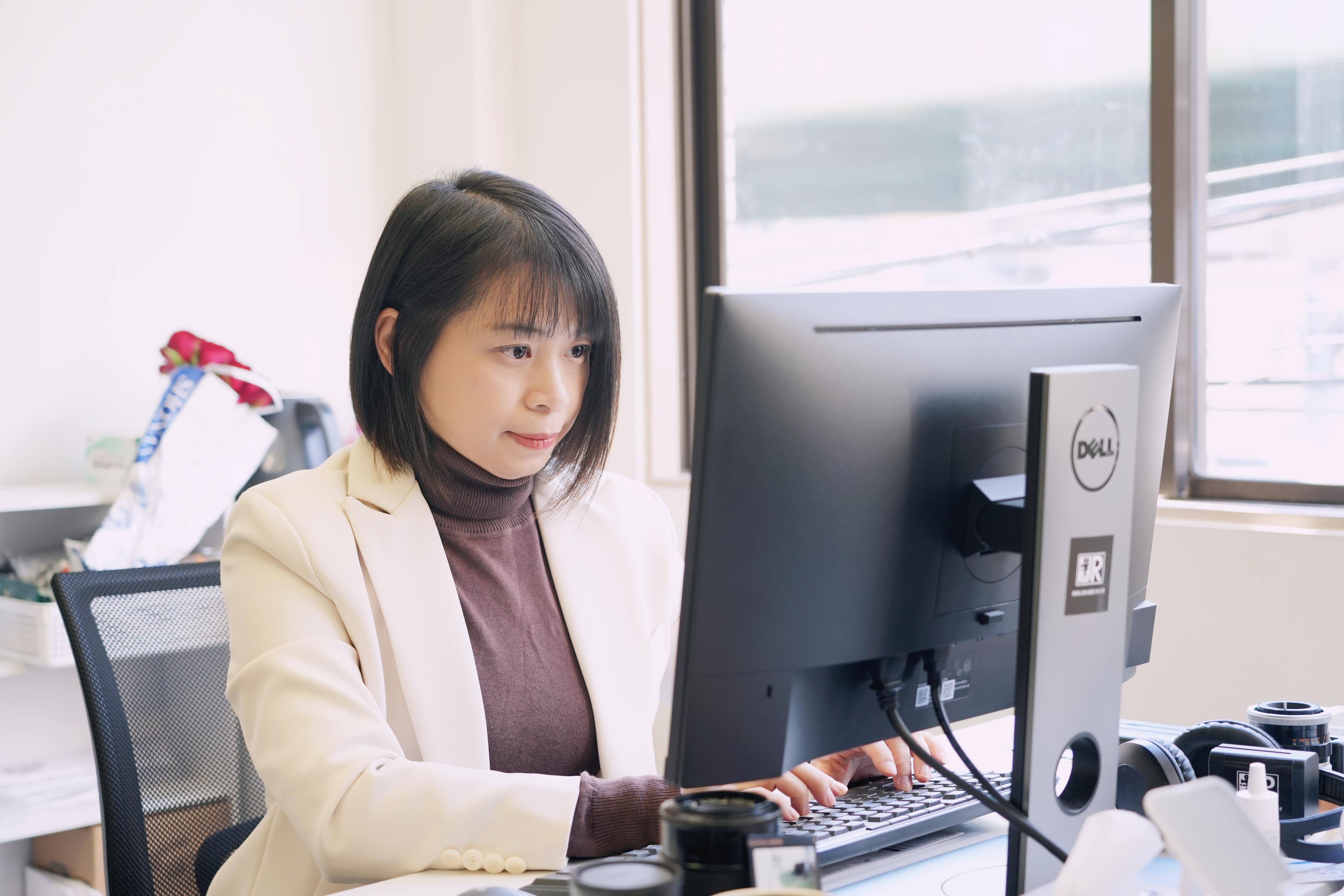 Liu Dong sits on a bright light office desk and watches the monitor when editing a video.