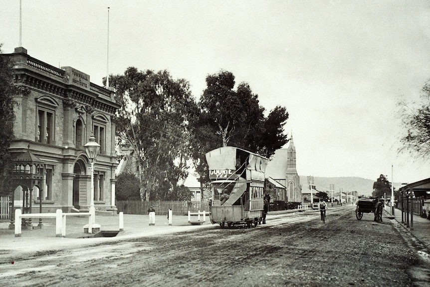 A black and white photo of a horse-drawn tram in front of old buildings