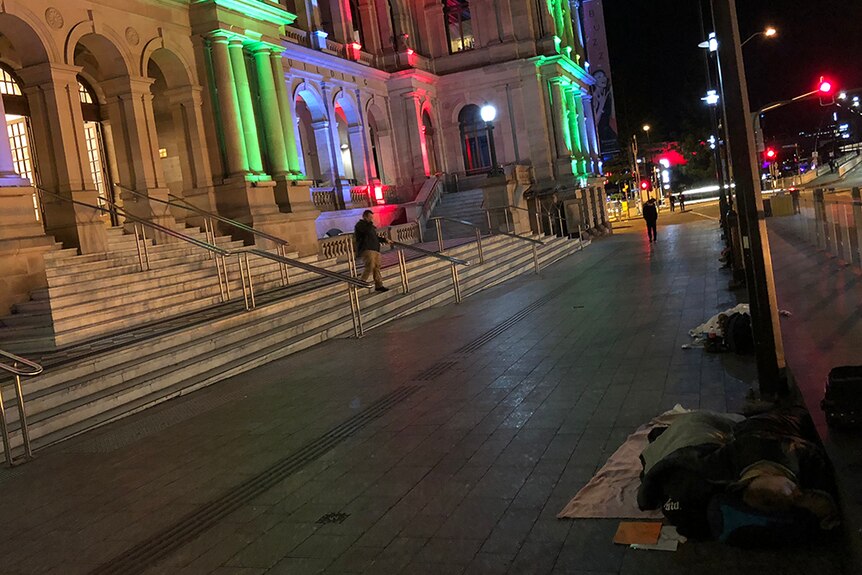 Two people sleeping rough on a cement pathway in front of the Treasury Casino in Brisbane.