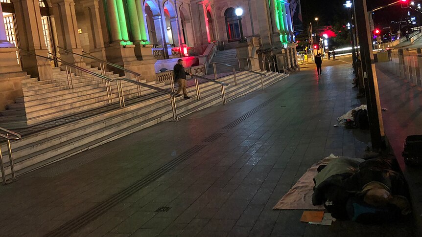 Two people sleeping rough on a cement pathway in front of the Treasury Casino in Brisbane.
