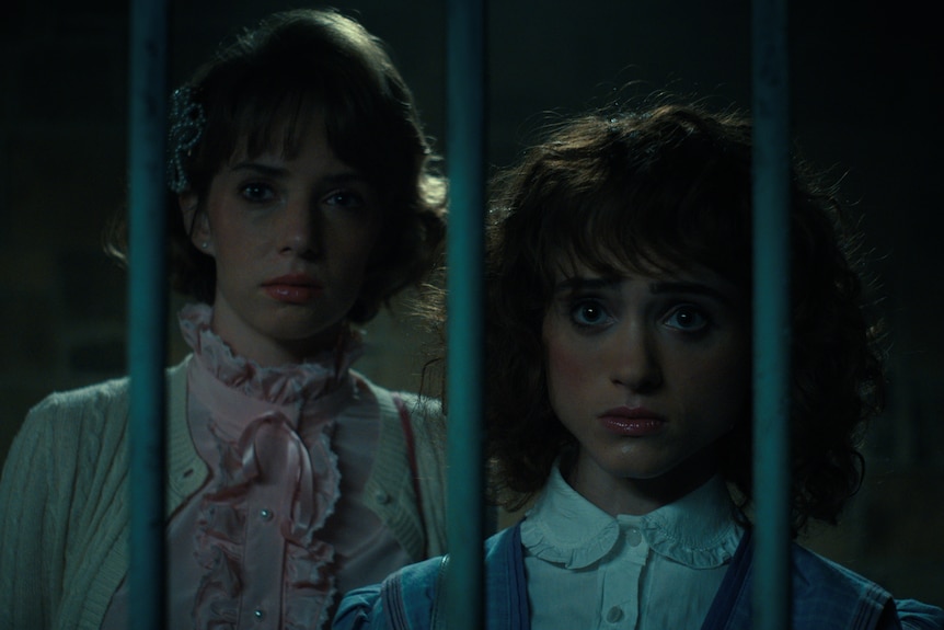 Two teens in formal 80s cloths look scared behind bars