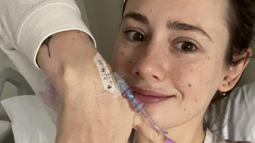 Woman with manicures hands smiles and holds up wrist to show canula 