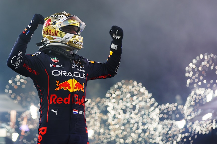 An F1 driver, in full suit and helmet, standing on his car, arms raised in celebration, while fireworks explode in the night sky