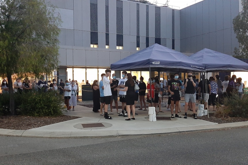 A wide shot showing a crowd of students and adults outside Fiona Stanley Hospital's COVID clinic waiting to get tested.