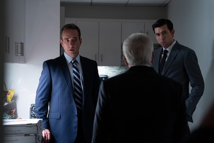 Still from TV show Succession: A man in his late 40s and a tall man in his early 30s, both in suits, the back of a shorter man