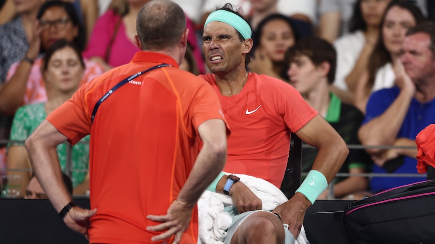 Rafael Nadal sitting appearing to be in pain with his hands on his hips. 