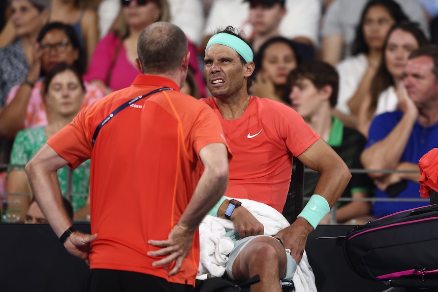 Rafael Nadal sitting appearing to be in pain with his hands on his hips. 