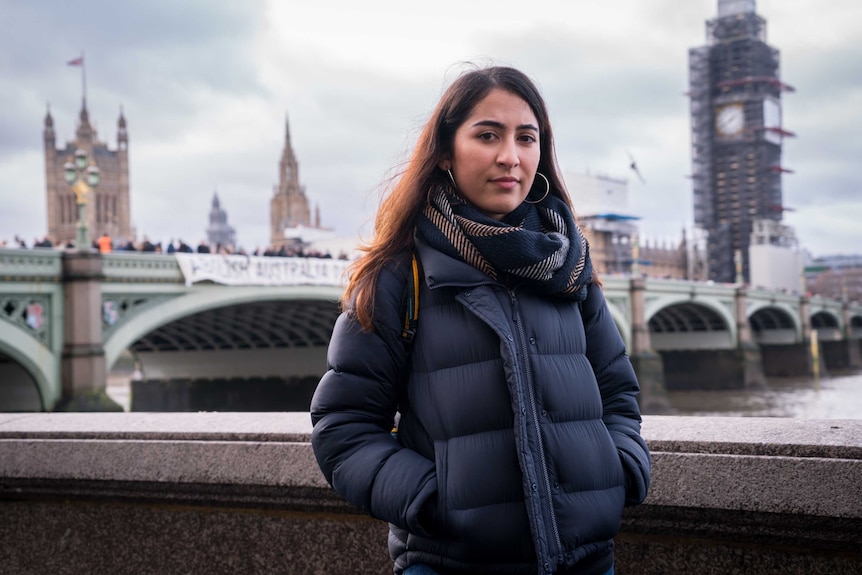 A woman dressed in a warm coat stands in front of the Westminster Bridge protest.