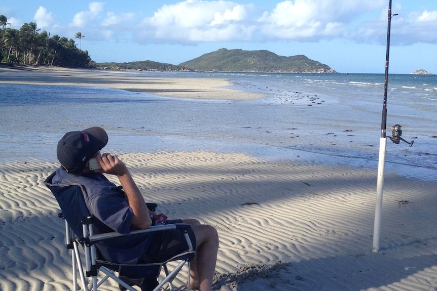 A man sits in a deck chair on a remote sandy beach in far north Queensland