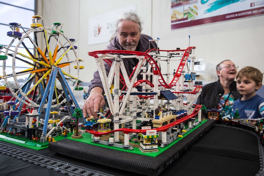 A man fiddles with a Lego rollercoaster, watched by a young boy and a woman.