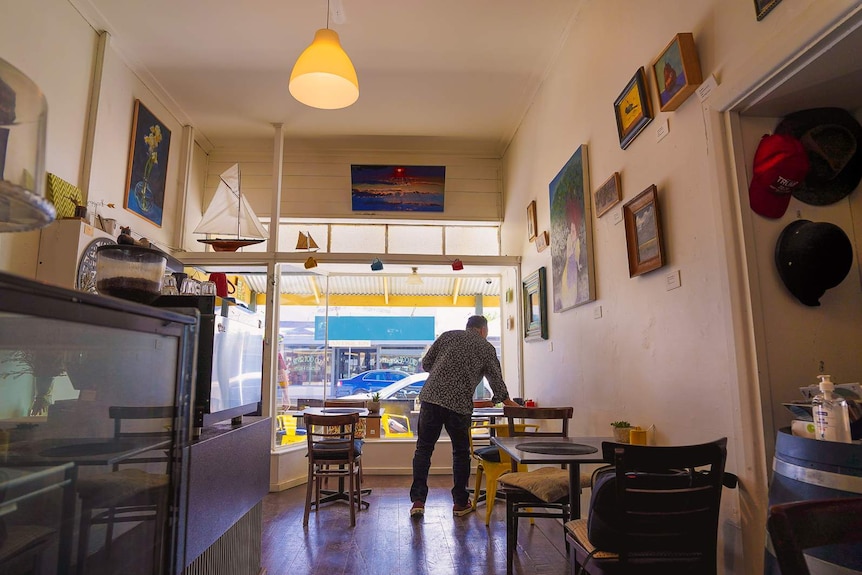 A man clears a table in a small, brightly lit and vibrantly decorated cafe space.
