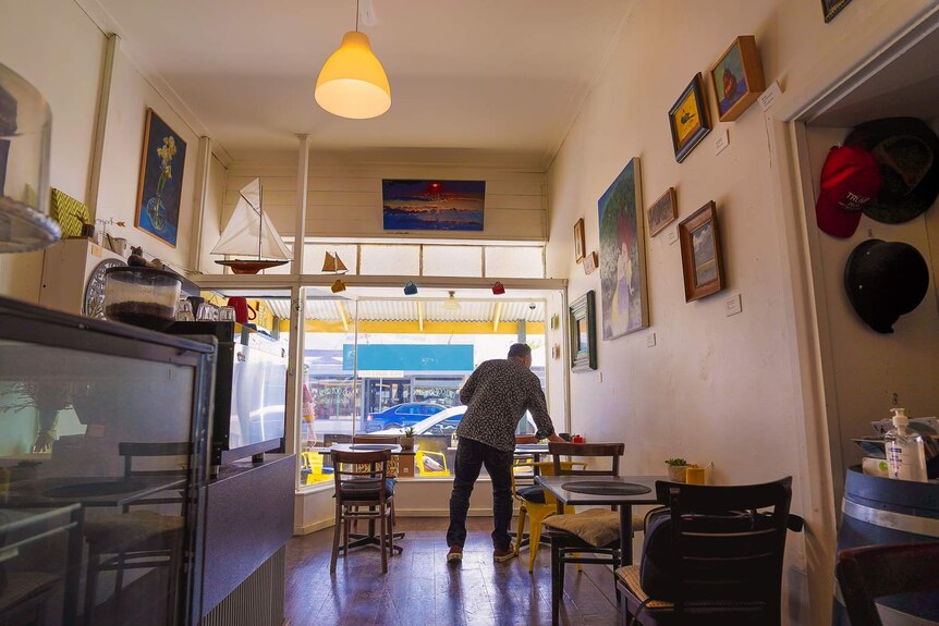 A man clears a table in a small, brightly lit and vibrantly decorated cafe space.