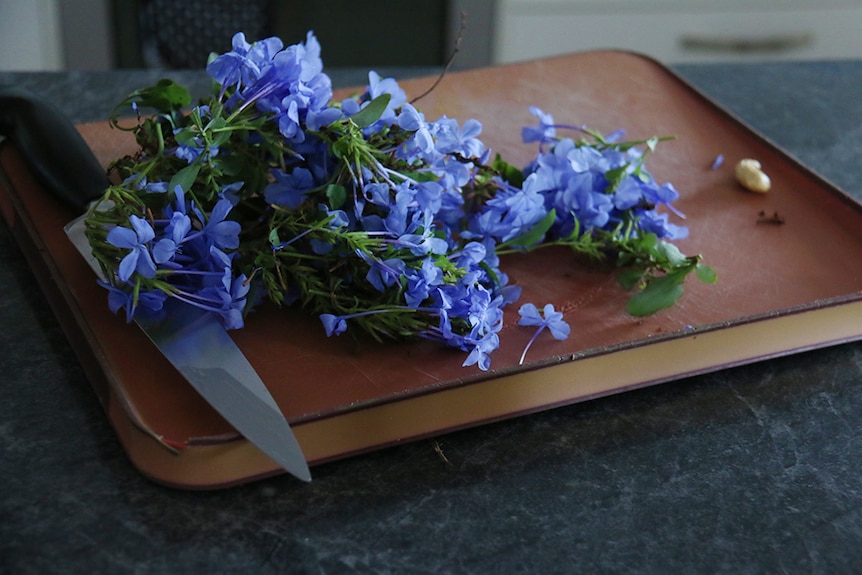 A bunch of lilac flowers on a brown chopping board laying next to a black-handled knife.