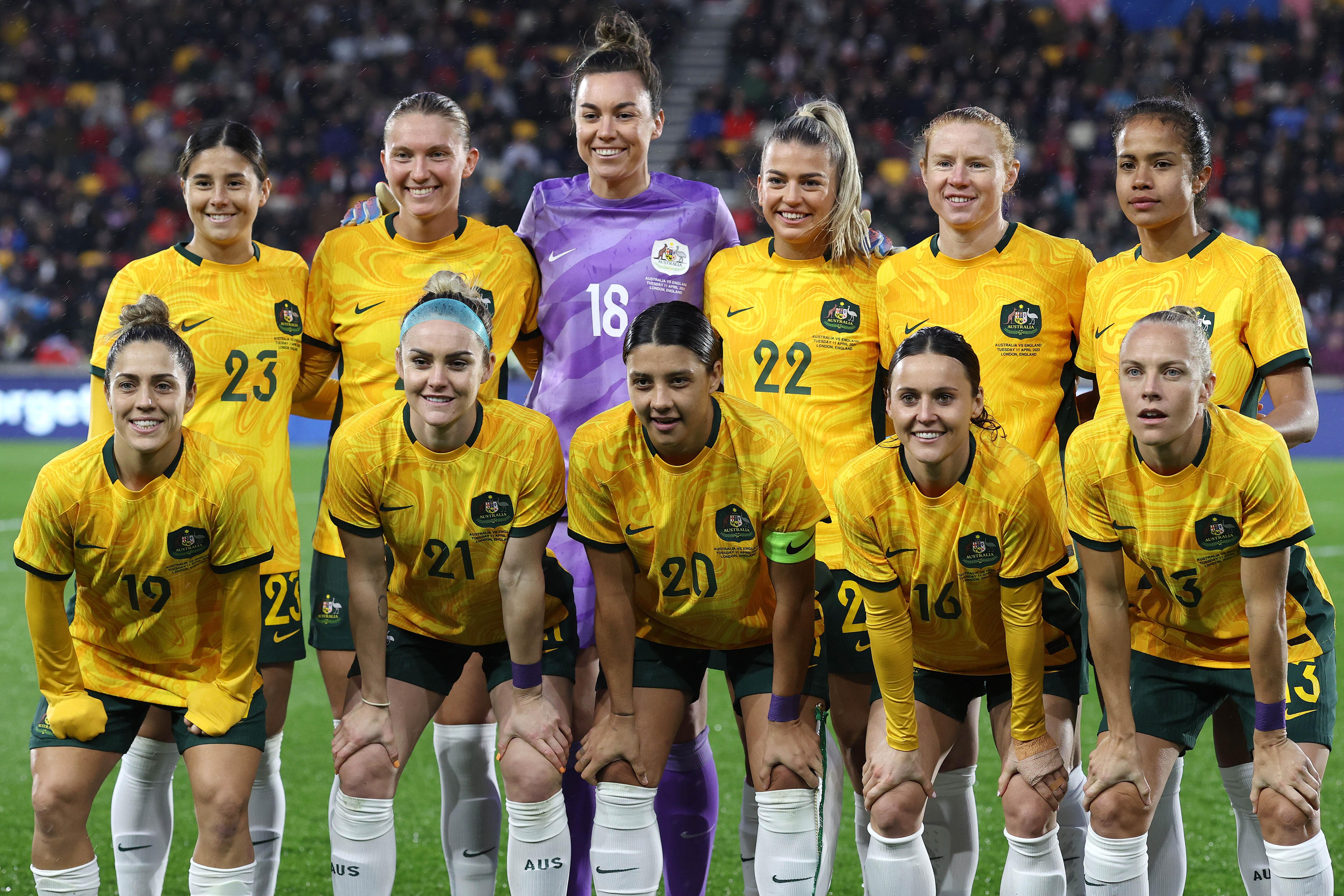 A soccer team wearing yellow and green uniforms stand in two rows for a photo before a match