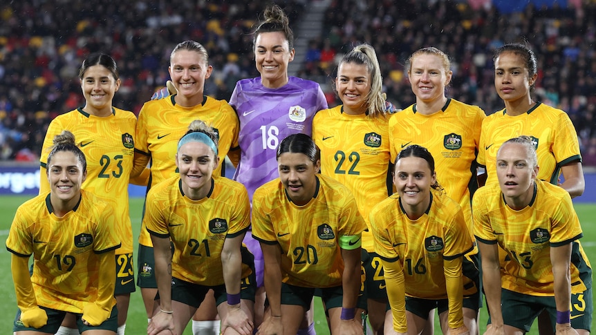 A soccer team wearing yellow and green uniforms stand in two rows for a photo before a match