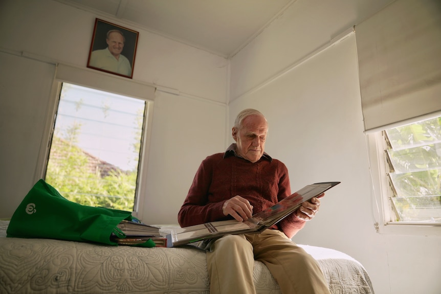 A man sits on a bed, looking at photo albums. 