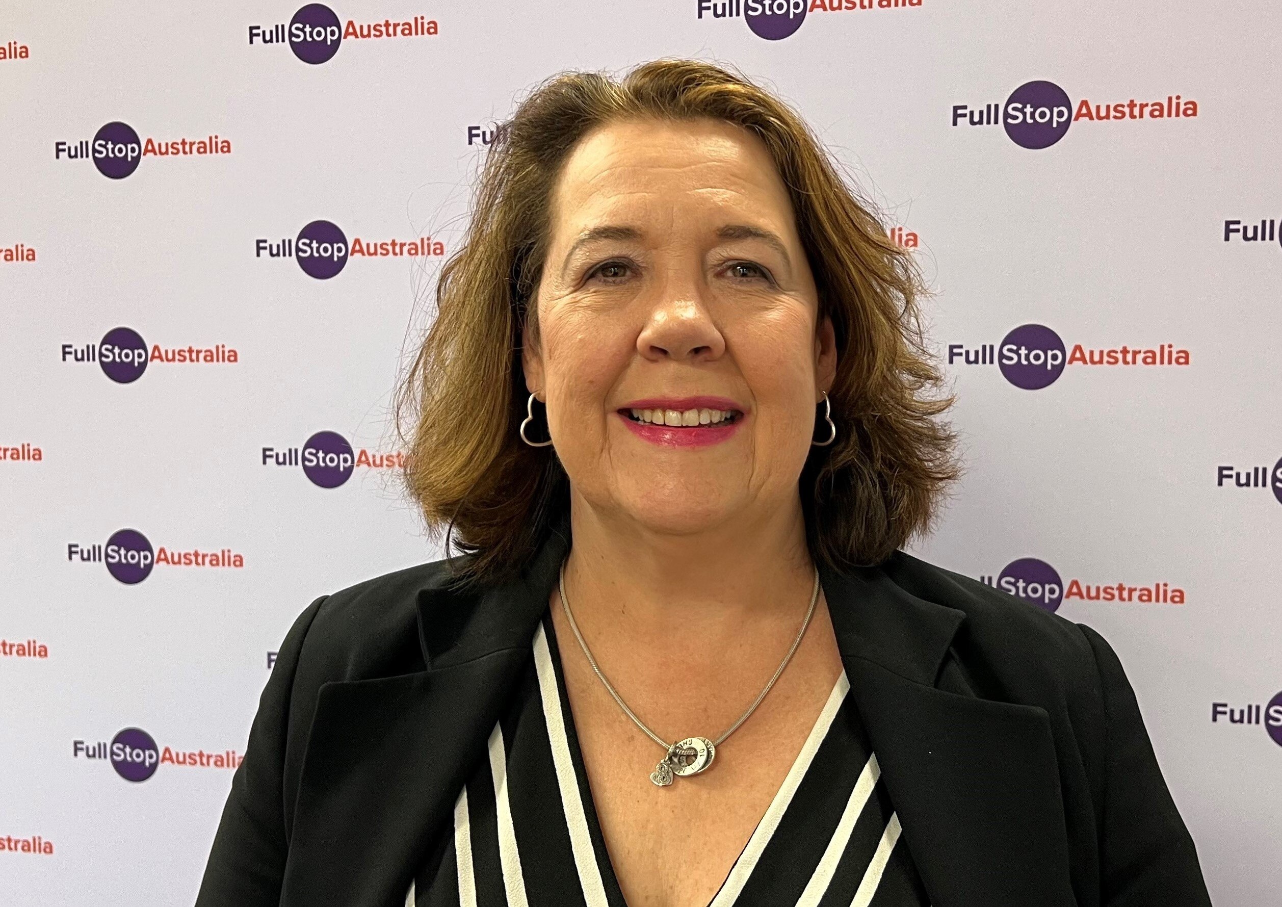 A woman standing in front of a banner that reads Full Stop Australia. 