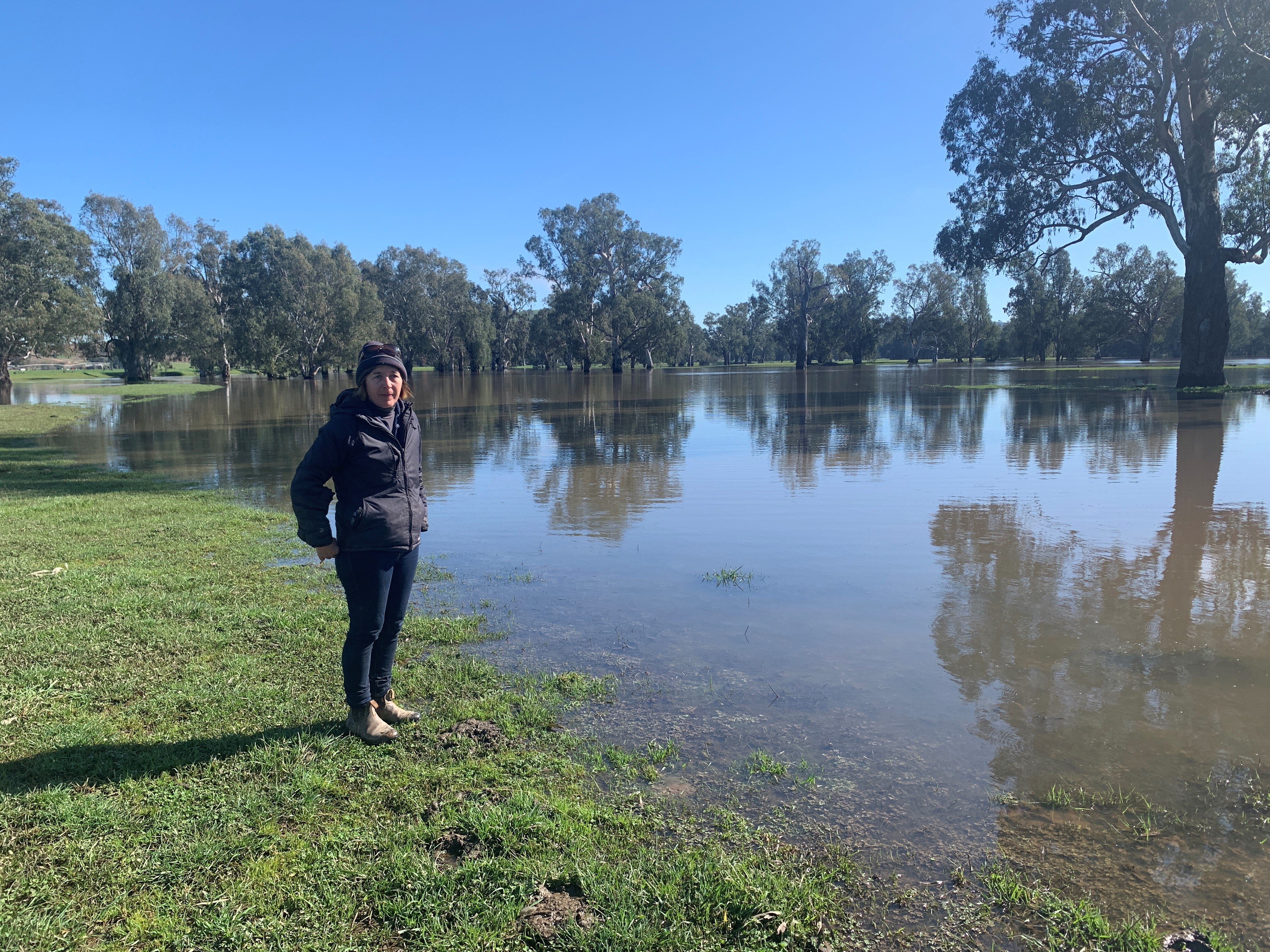A woman stands in front of floodwaters, spread out across paddocks. 