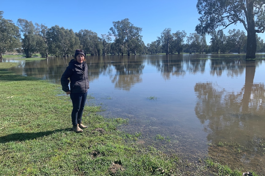 A woman stands in front of floodwaters, spread out across paddocks. 