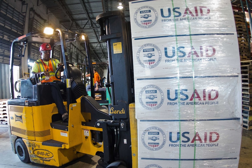 Forklifts move pallets of supplies at a USAID shipping and logistics facility in Miami.