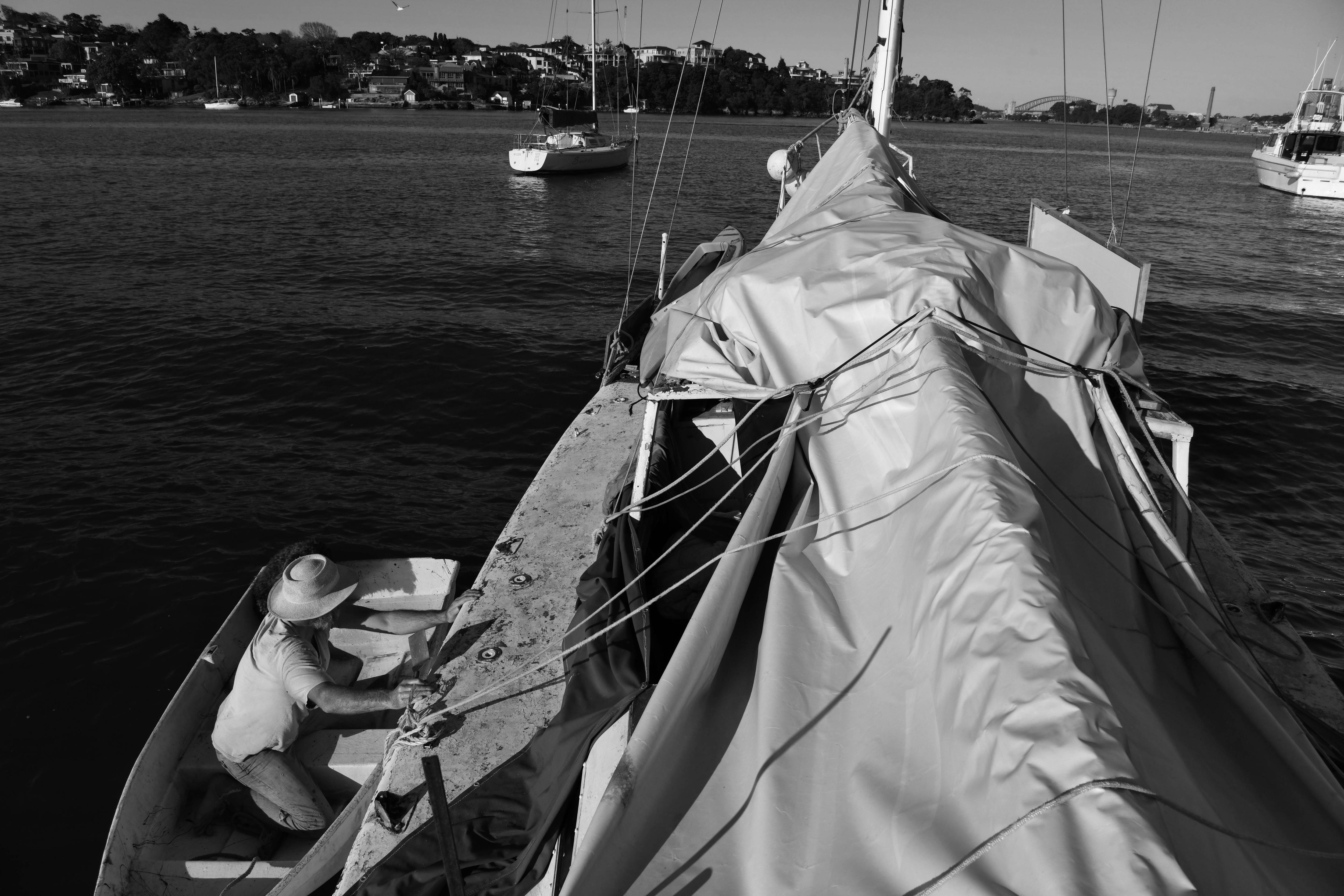 A man covers a yacht with tarp from his dinghy