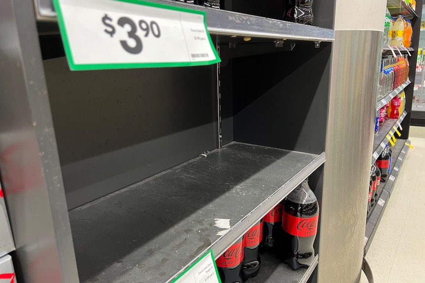 An empty supermarket shelf about a shelf of coke bottles