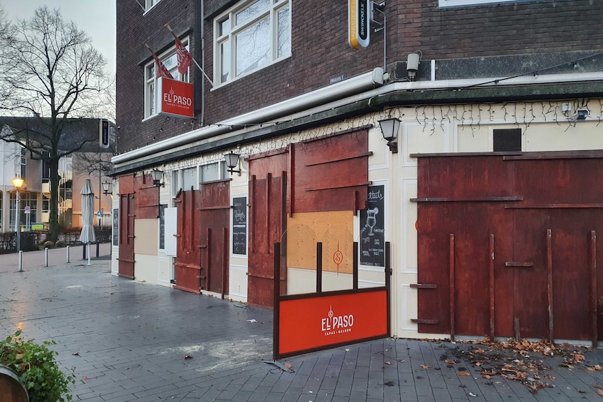 A boarded up shop at the front of a brick building on a wintry European street with debris in front.