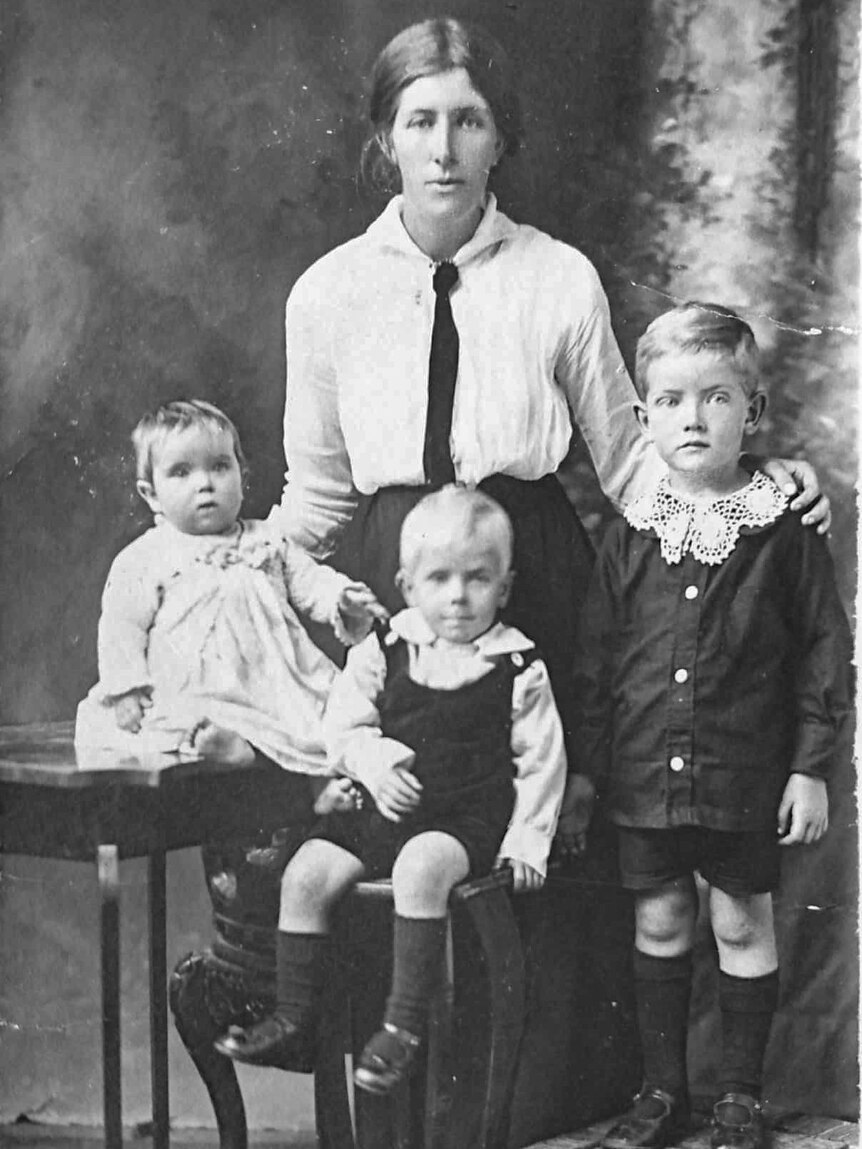 A black and white photo of a mother and her three children posing for a photograph.