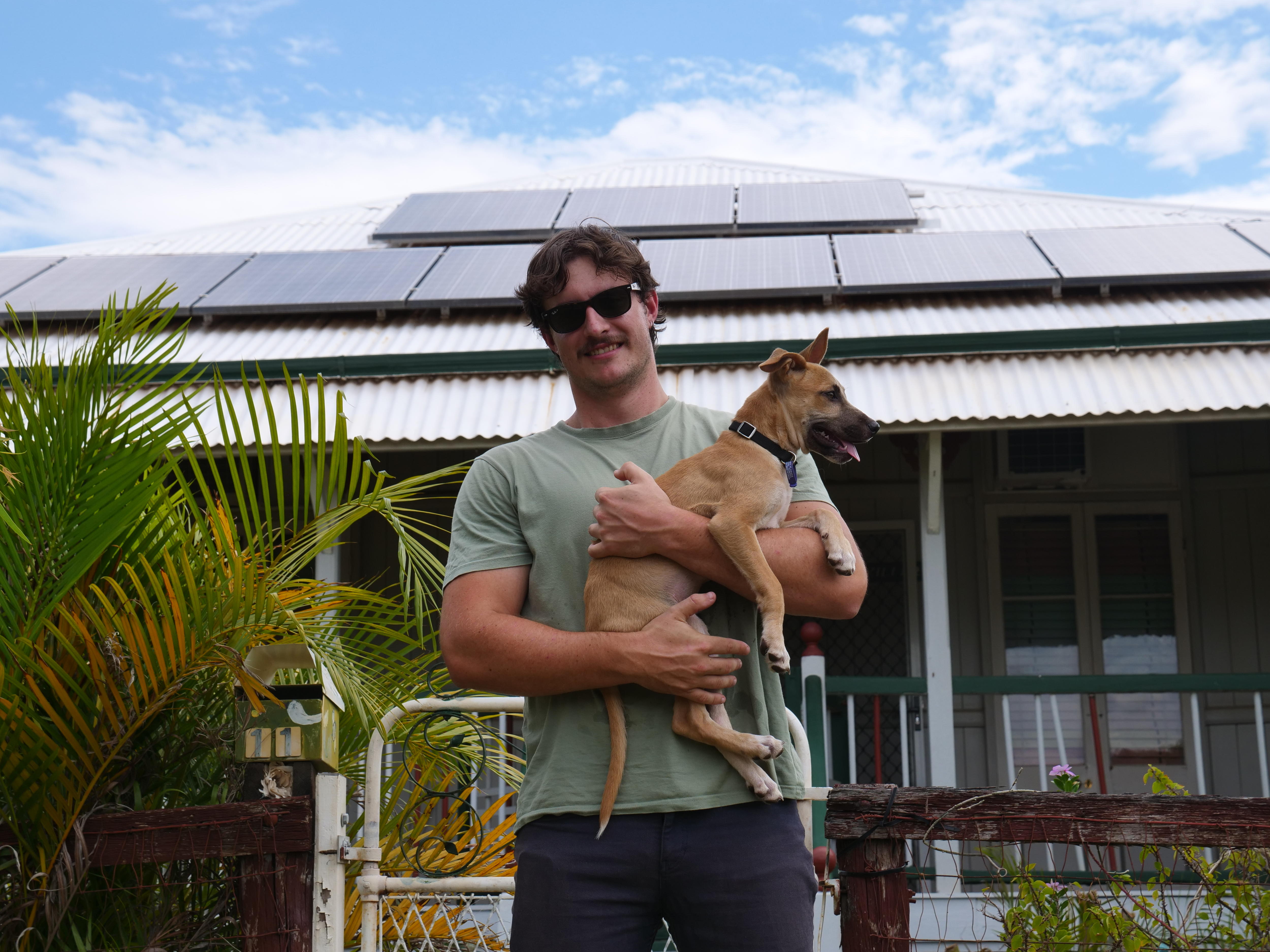 Hombre sonriendo y sosteniendo un perro frente a la casa