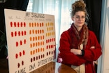 A woman stands next to a sign saying "my siblings"